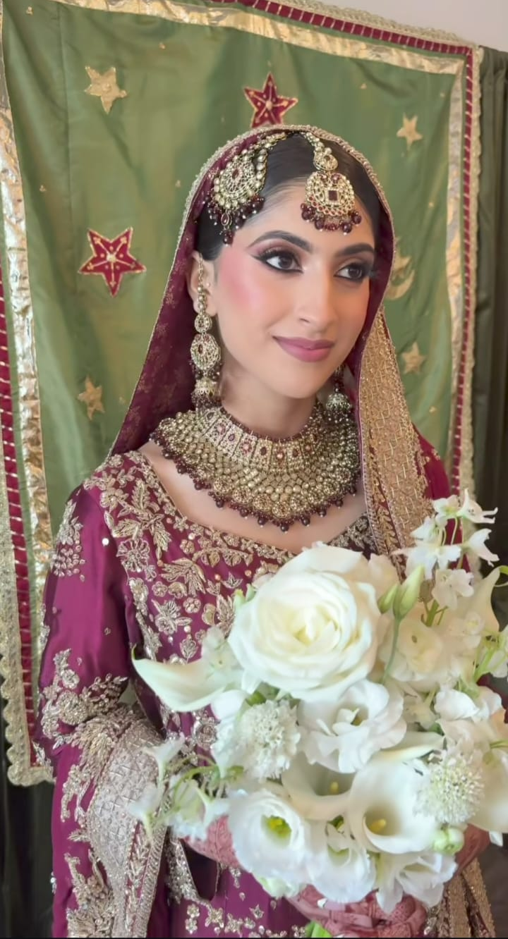Pakistani American Bride holding a bouquet of white flowers, standing in front of handmade backdrop by zar 